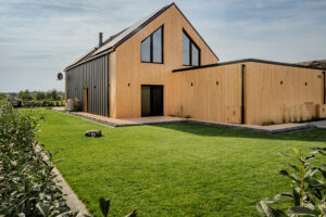 Usługi Ogrodnicze Krobia - widok ogrodu z zadbanym trawnikiem i żywopłotem z laurowiśni przy nowoczesnej zabudowie.