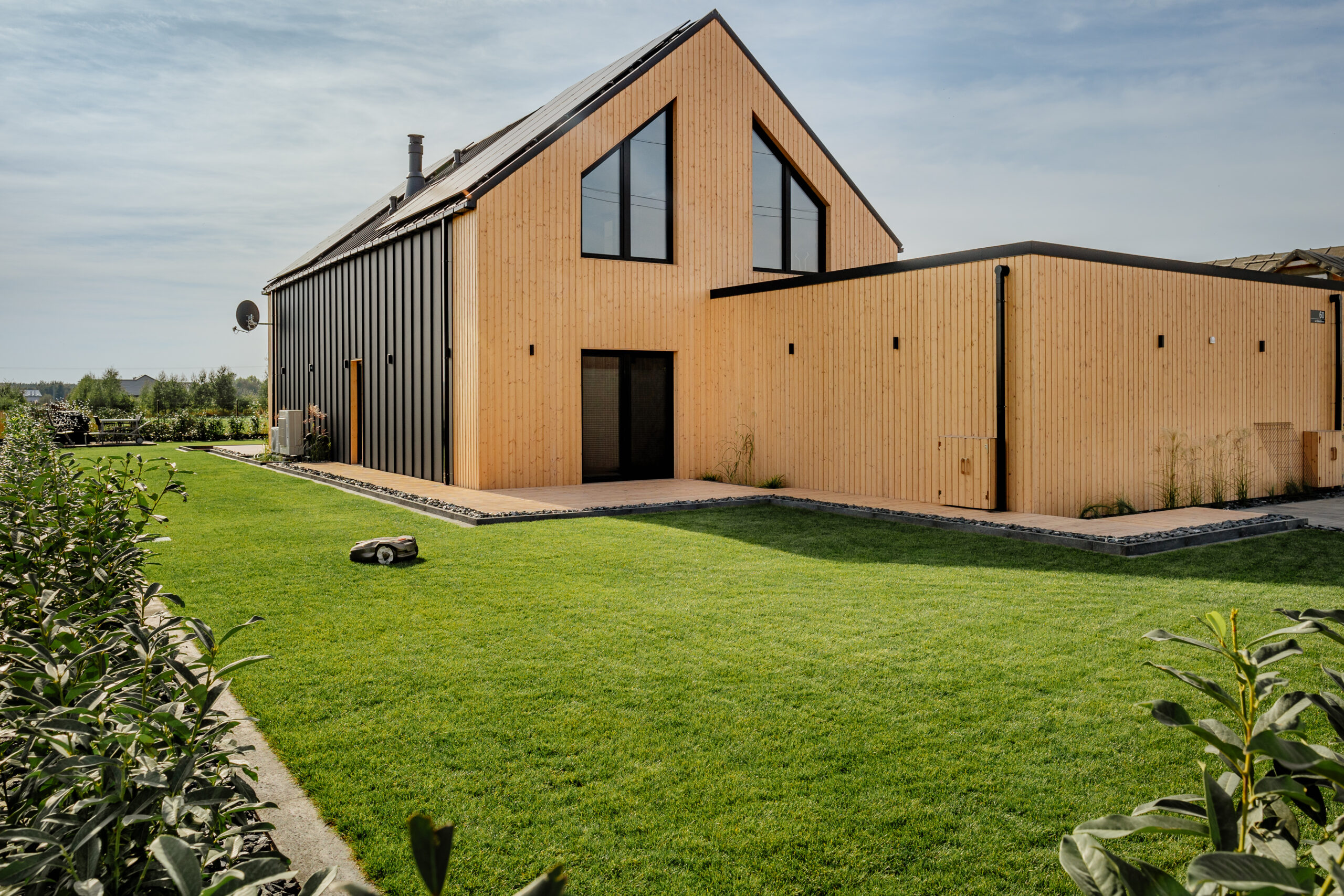 Usługi Ogrodnicze Krobia - widok ogrodu z zadbanym trawnikiem i żywopłotem z laurowiśni przy nowoczesnej zabudowie.