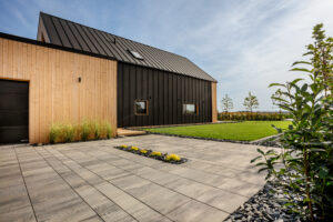 Usługi ogrodnicze Krobia - podjazd z nowoczesnej kostki brukowej w większym formacie, z rabatami z traw i zielonym zadbanym trawnikiem