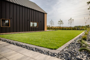 Usługi ogrodnicze Krobia - zielony trawnik w towarzystwie rabaty wykończonej korą z fyllitu.